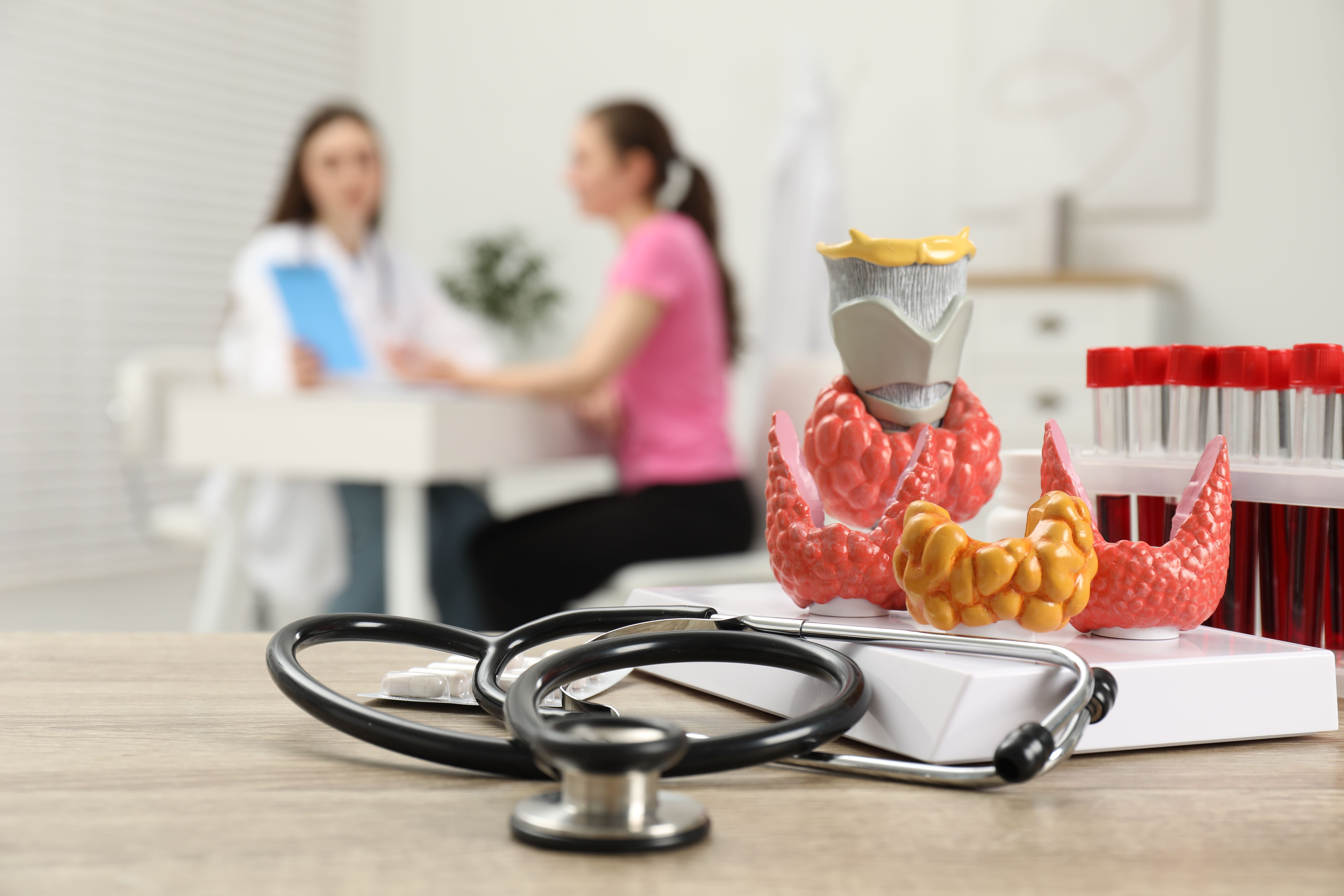 An endocrinologist consulting with a patient in a clinic, with anatomical models and medical tools visible.