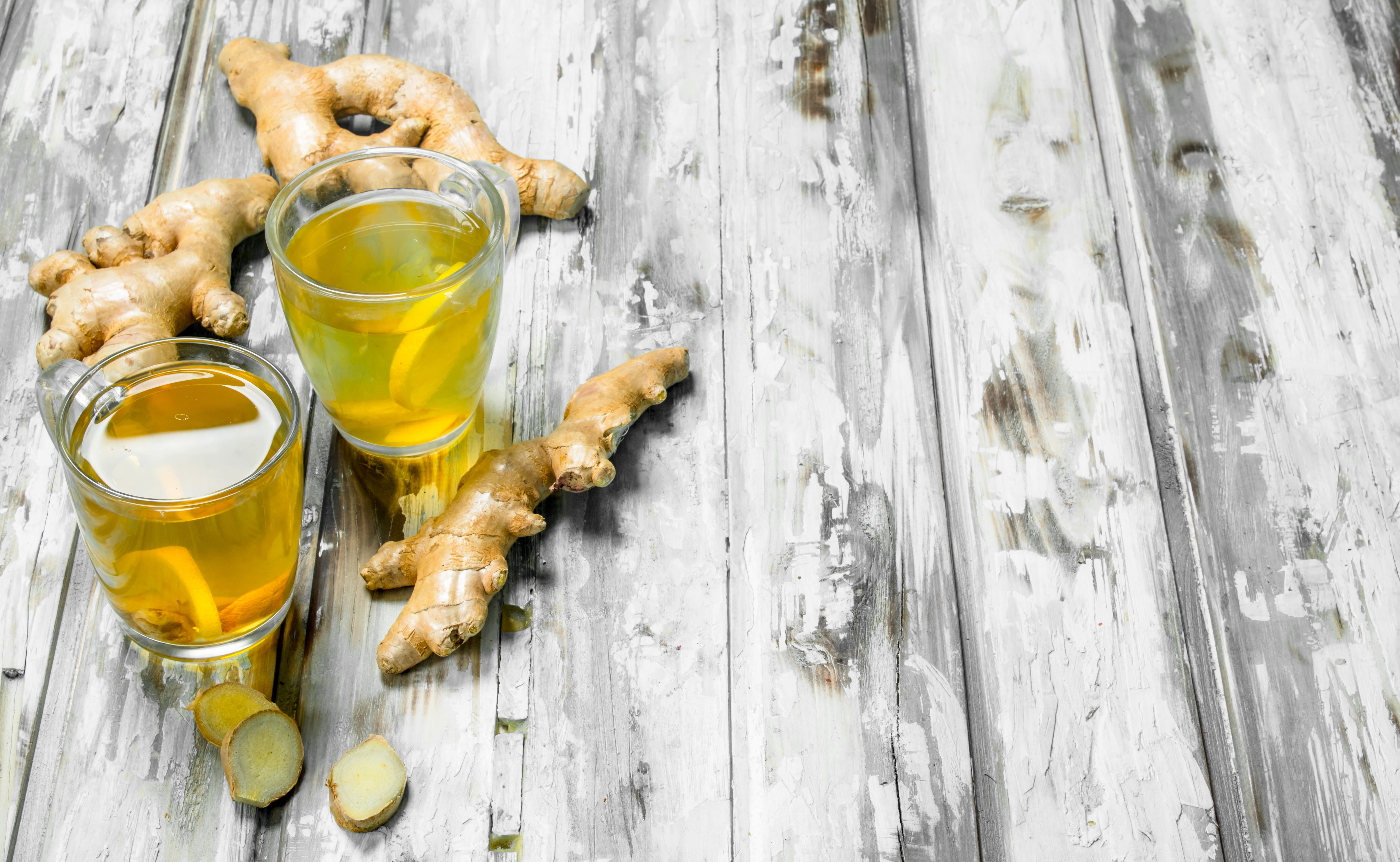 Two glasses of ginger tea beside fresh ginger roots on a wooden table.
