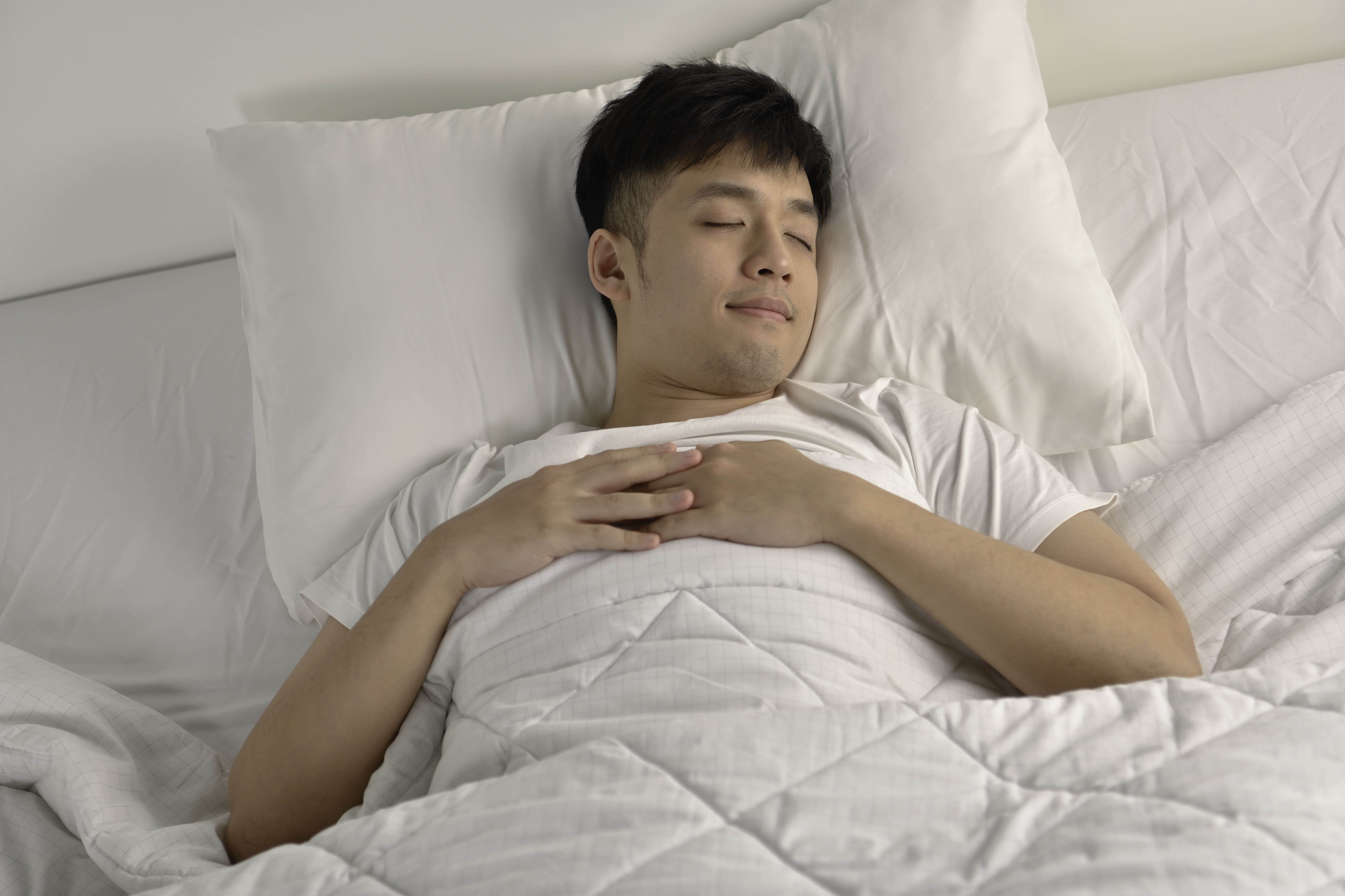 A peaceful young man sleeping comfortably in bed, with a white blanket, demonstrating relaxation.